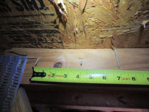 Photo of a tape measure extended across a roof truss with several exposed nails.