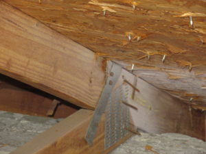 A metal strap nailed to the roof truss for wind mitigation.